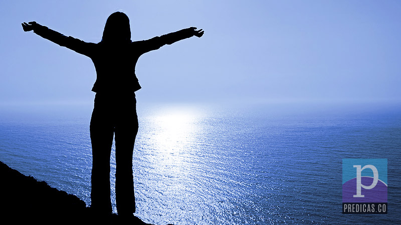 Mujer cristiana levanta sus manos frente al mar